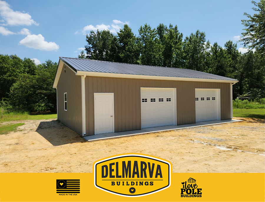Tan pole barn with metal roof, two white garage doors, and side entry door by Delmarva Buildings.