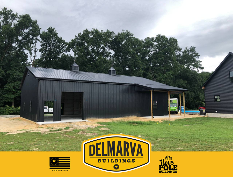 Black pole barn under construction with metal roof, garage door, and covered porch.