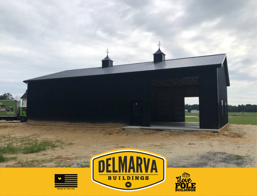 Black pole barn with cupolas, metal roof, and open bays.