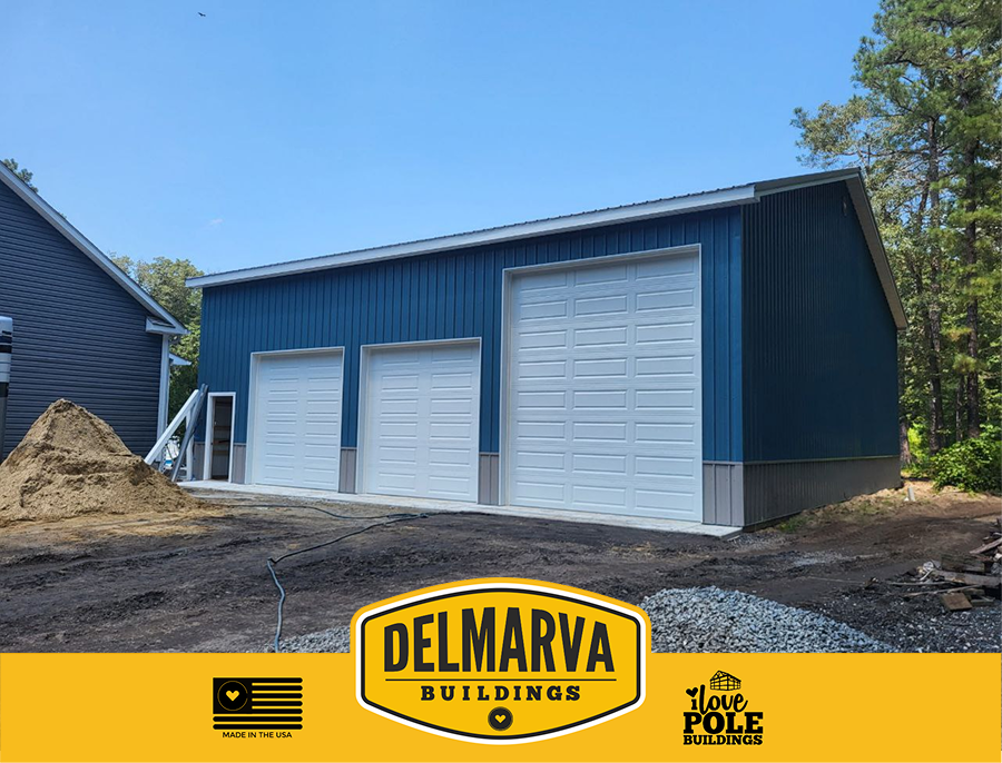 Blue pole barn three-bay garage with white doors and gray trim.