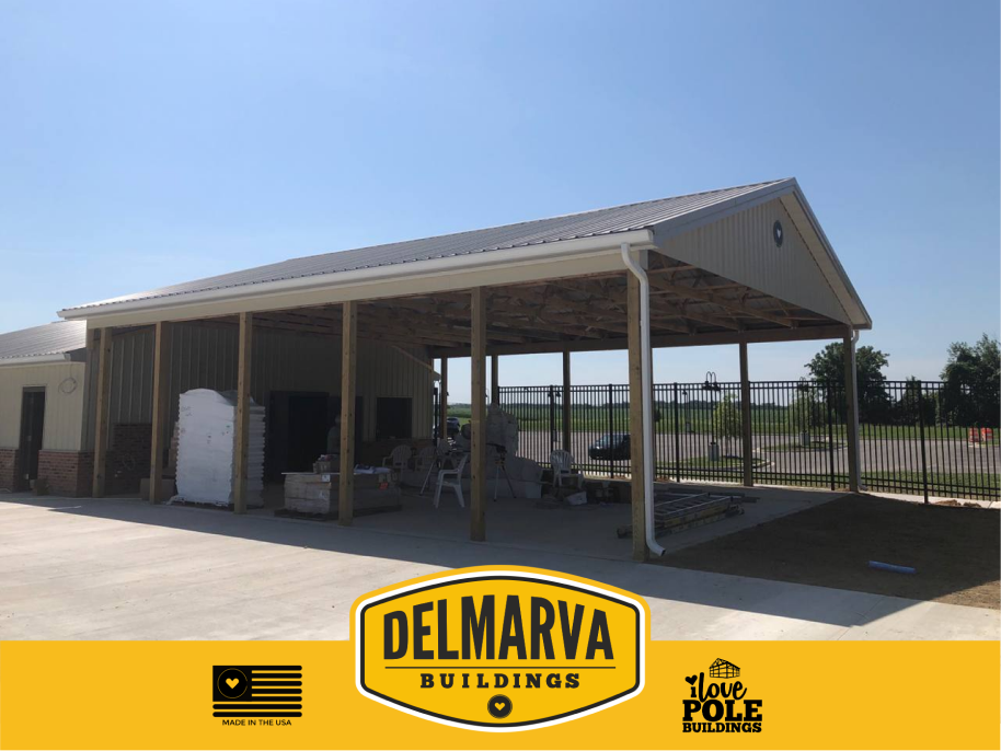 Tan and gray pole barn with metal roof and large open covered shelter area by Delmarva Buildings.