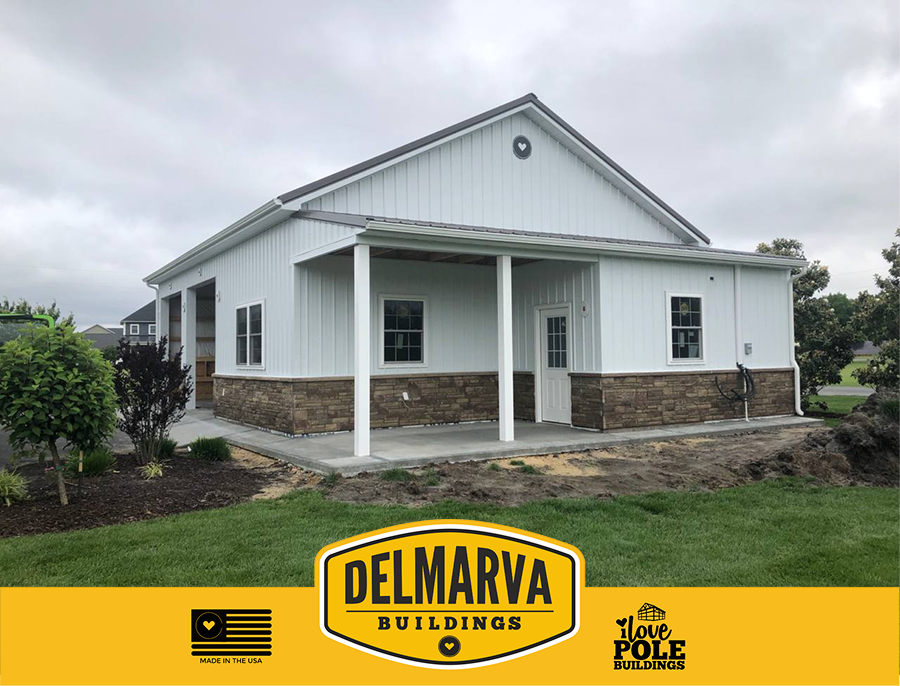 White pole barn house with stone base, covered porch, and multiple windows by Delmarva Buildings.