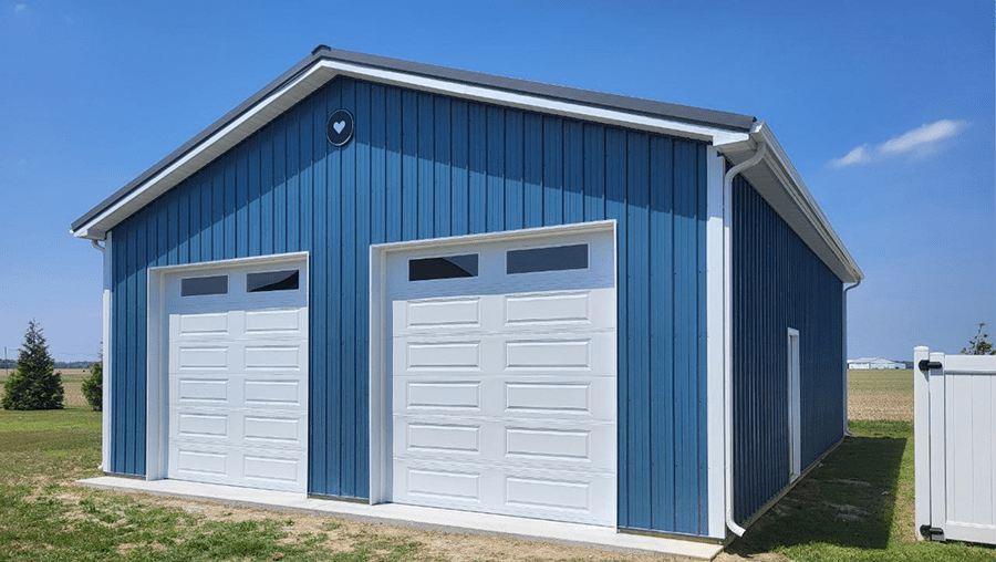 Blue pole barn with two white garage doors and white trim by Delmarva Buildings.