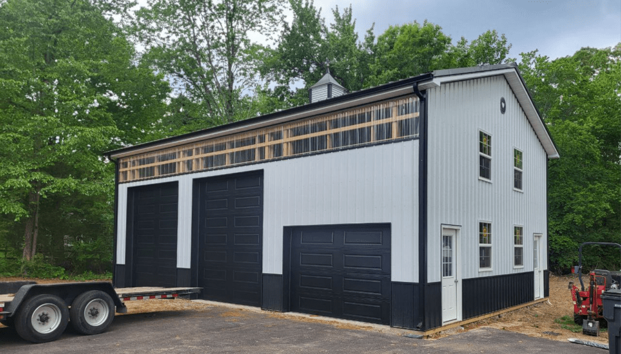 White and black pole barn with three black garage doors, cupola, and wood trim by Delmarva Buildings.
