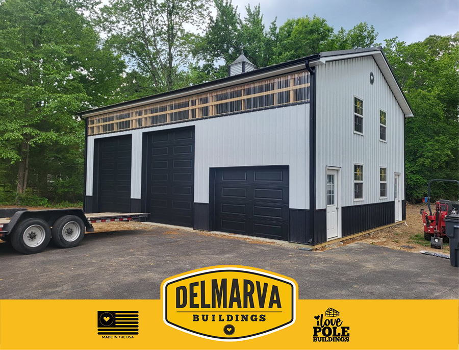 White and black pole barn with three black garage doors, cupola, and wood trim by Delmarva Buildings.