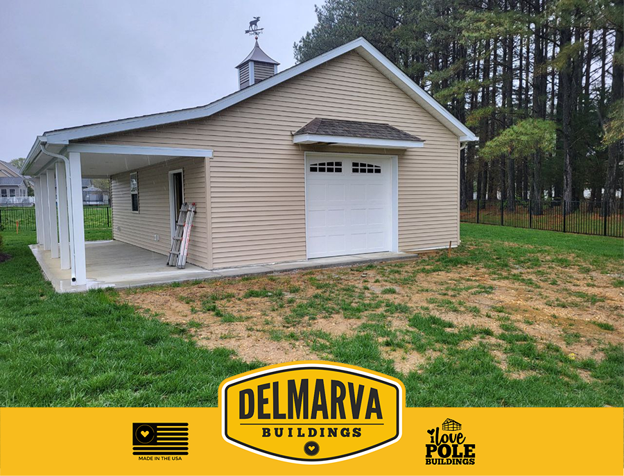 Tan pole barn with white garage door, cupola, and a porch by Delmarva Buildings.