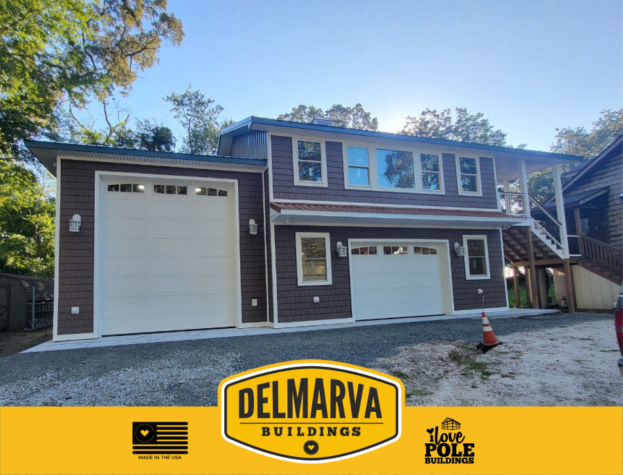 Dark gray pole building house with two-bay garage, white doors, and covered deck by Delmarva Buildings.