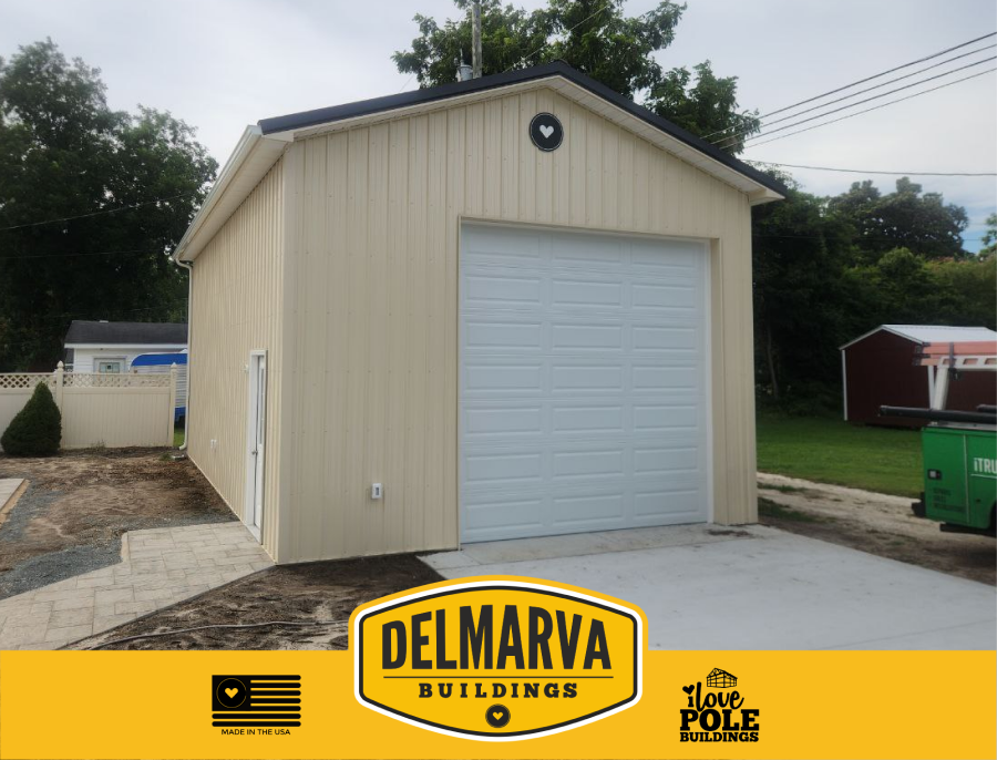 Cream pole barn with black roof and white garage door by Delmarva Buildings.